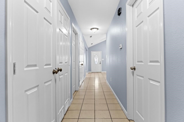 hall featuring light tile patterned floors, baseboards, and vaulted ceiling