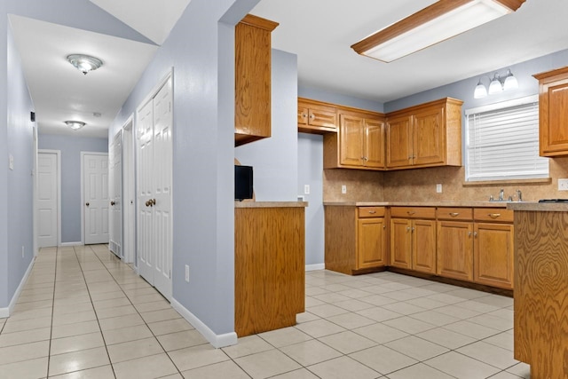 kitchen with brown cabinetry, light tile patterned flooring, light countertops, and tasteful backsplash