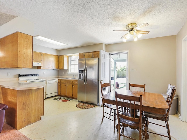 kitchen featuring brown cabinets, light floors, light countertops, white appliances, and under cabinet range hood