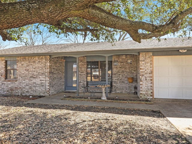 doorway to property with a garage, brick siding, and roof with shingles