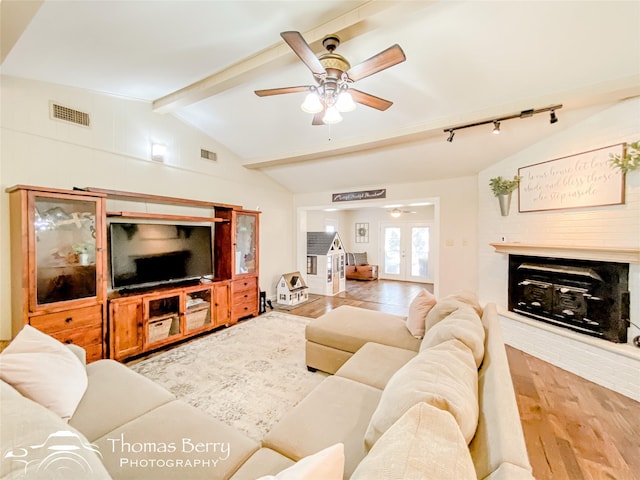 living room with french doors, vaulted ceiling with beams, visible vents, a glass covered fireplace, and wood finished floors