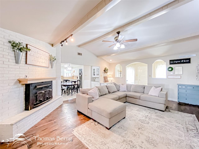 living area featuring arched walkways, vaulted ceiling with beams, visible vents, ceiling fan, and wood finished floors