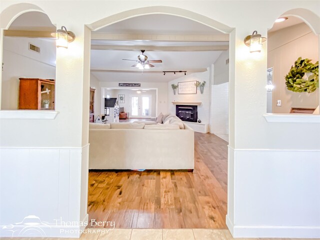 unfurnished living room with visible vents, a fireplace with raised hearth, light wood-style floors, ceiling fan, and beamed ceiling