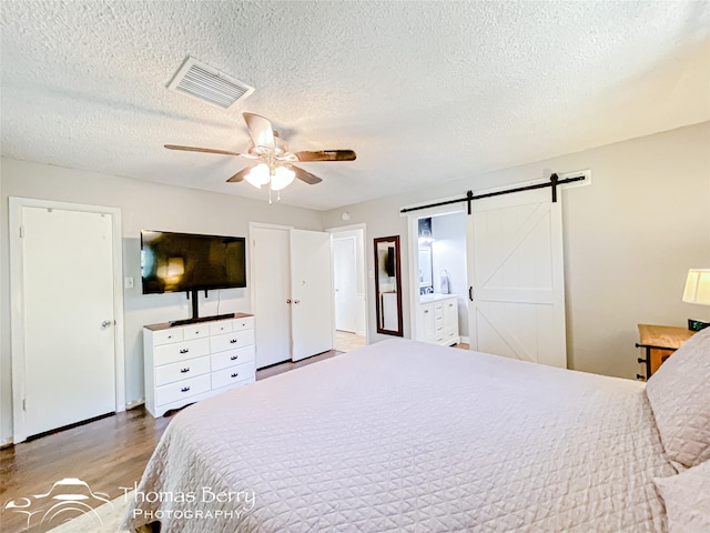 bedroom featuring visible vents, light wood-style flooring, a barn door, a ceiling fan, and a textured ceiling