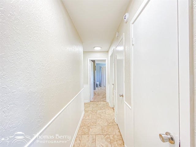 hall featuring a wainscoted wall, a decorative wall, and a textured wall