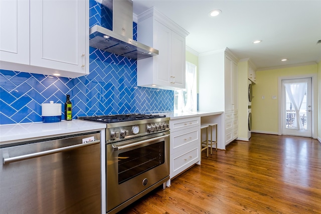 kitchen with crown molding, appliances with stainless steel finishes, stacked washer / dryer, white cabinetry, and wall chimney exhaust hood