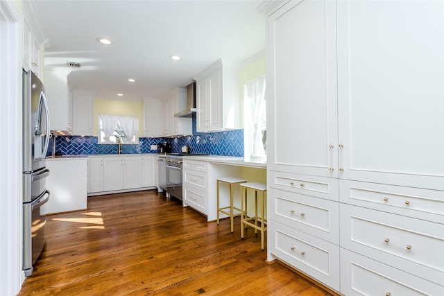 kitchen featuring wall chimney exhaust hood, appliances with stainless steel finishes, dark wood finished floors, and decorative backsplash