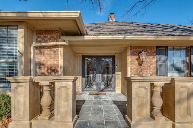 view of exterior entry featuring french doors, brick siding, and roof with shingles