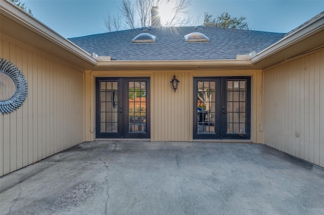 view of exterior entry featuring a patio area, roof with shingles, and french doors