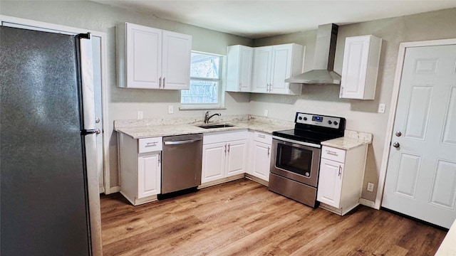 kitchen featuring light wood-type flooring, wall chimney range hood, white cabinetry, and appliances with stainless steel finishes