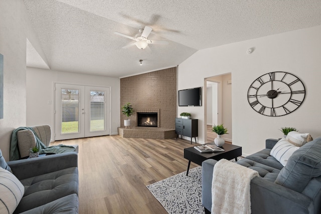 living room with a textured ceiling, light wood-style floors, vaulted ceiling, french doors, and a brick fireplace