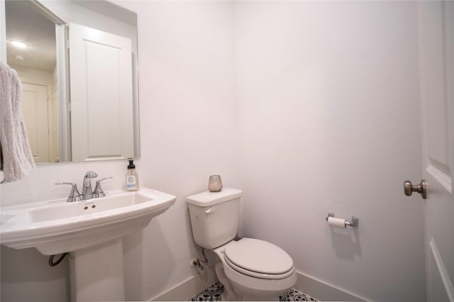 half bath featuring toilet, baseboards, and a sink