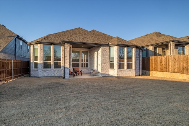 back of property featuring brick siding, a yard, roof with shingles, a patio area, and a fenced backyard