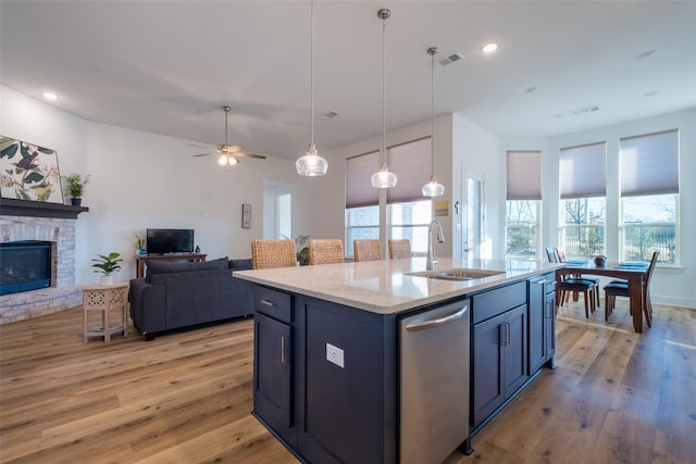 kitchen featuring a stone fireplace, a sink, open floor plan, stainless steel dishwasher, and light wood-type flooring