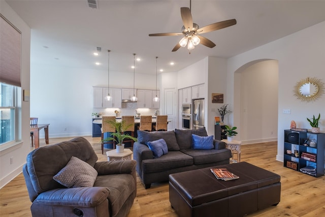 living room featuring arched walkways, recessed lighting, visible vents, light wood-style flooring, and baseboards