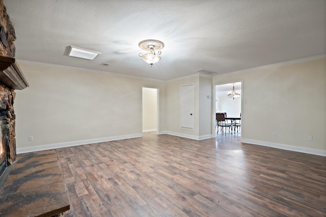 unfurnished living room with ornamental molding, wood finished floors, an inviting chandelier, a textured ceiling, and a stone fireplace