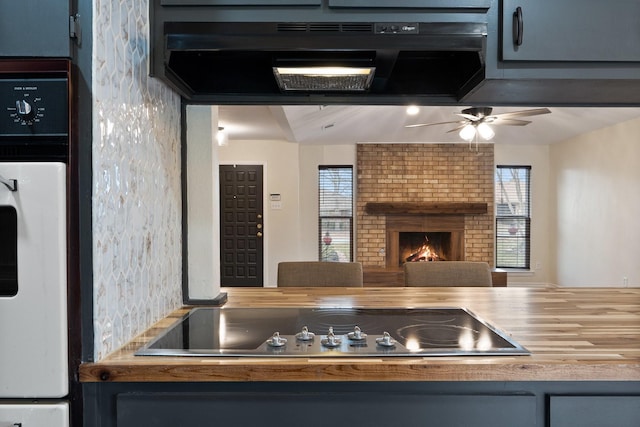 kitchen with oven, extractor fan, black electric cooktop, a fireplace, and a wealth of natural light