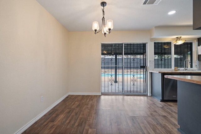 unfurnished dining area with wood finished floors, an inviting chandelier, a sink, and baseboards