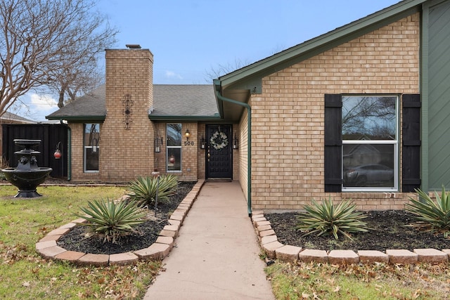 property entrance featuring roof with shingles, brick siding, and a chimney