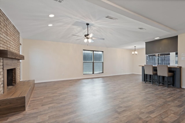 unfurnished living room featuring baseboards, visible vents, wood finished floors, a fireplace, and ceiling fan with notable chandelier