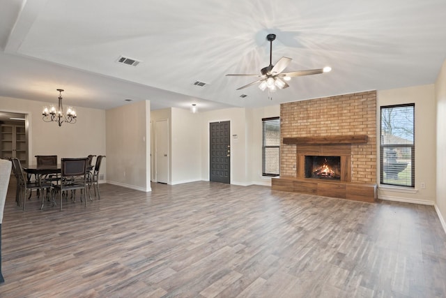 living area featuring visible vents, a brick fireplace, wood finished floors, baseboards, and ceiling fan with notable chandelier