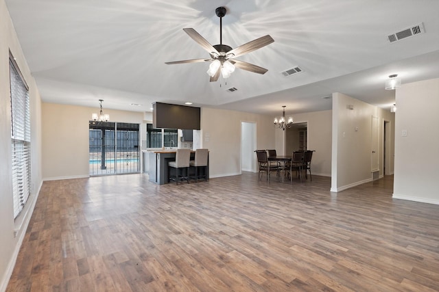 unfurnished living room with ceiling fan with notable chandelier, visible vents, and wood finished floors