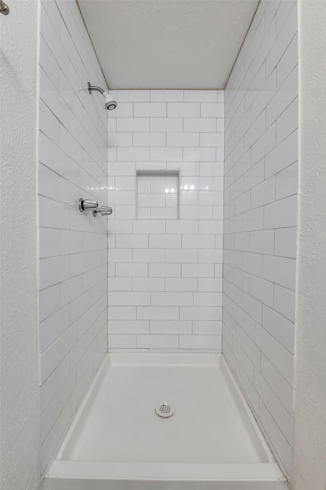 full bathroom featuring a stall shower, a textured wall, and a textured ceiling