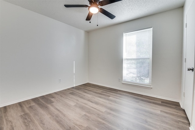 empty room with a textured ceiling, wood finished floors, a ceiling fan, and baseboards