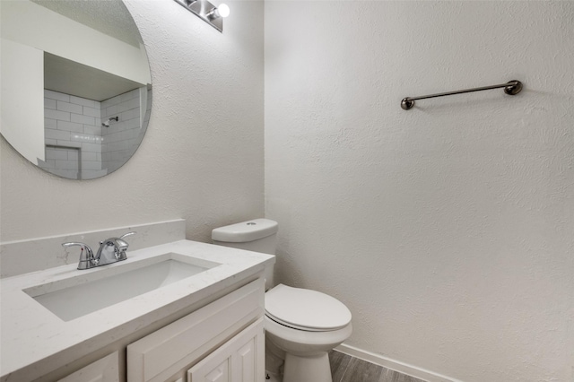 full bath featuring a textured wall, vanity, toilet, and wood finished floors