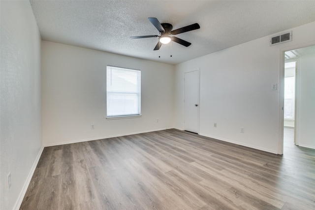 spare room with baseboards, a textured ceiling, visible vents, and wood finished floors