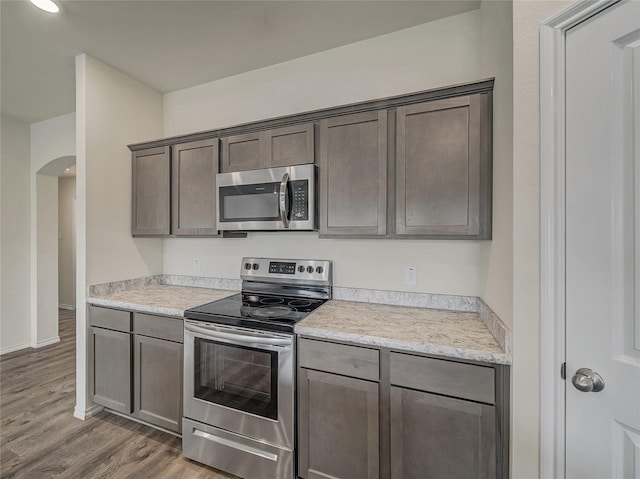 kitchen with arched walkways, light wood finished floors, light countertops, appliances with stainless steel finishes, and dark brown cabinets