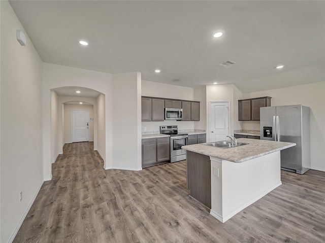 kitchen with arched walkways, stainless steel appliances, wood finished floors, and a sink