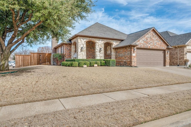 french country style house featuring an attached garage, brick siding, a shingled roof, concrete driveway, and stone siding