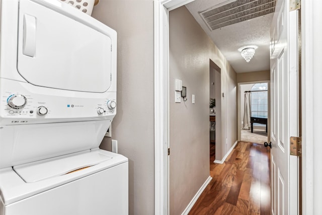 laundry area featuring stacked washer and clothes dryer, dark wood-style flooring, visible vents, laundry area, and baseboards