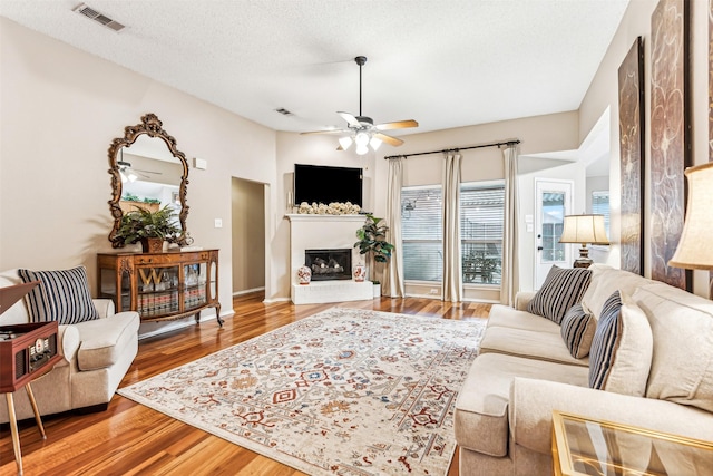 living area featuring visible vents, a ceiling fan, a brick fireplace, a textured ceiling, and wood finished floors