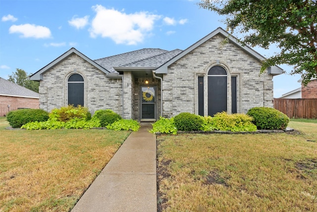 french country home with a shingled roof, fence, a front lawn, and brick siding