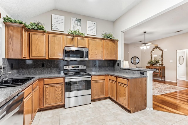 kitchen featuring stainless steel appliances, a peninsula, a sink, brown cabinets, and decorative backsplash