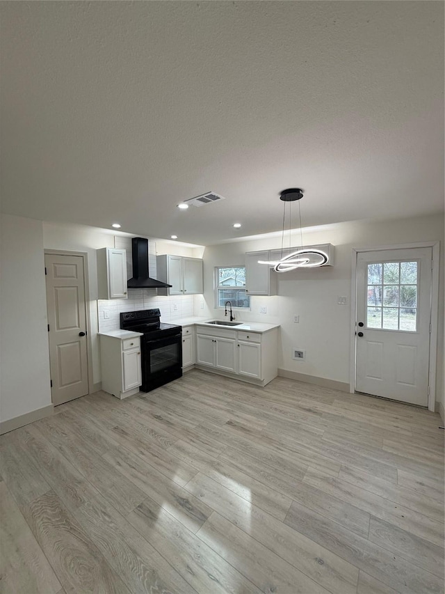 kitchen with light wood finished floors, visible vents, wall chimney exhaust hood, black / electric stove, and a sink