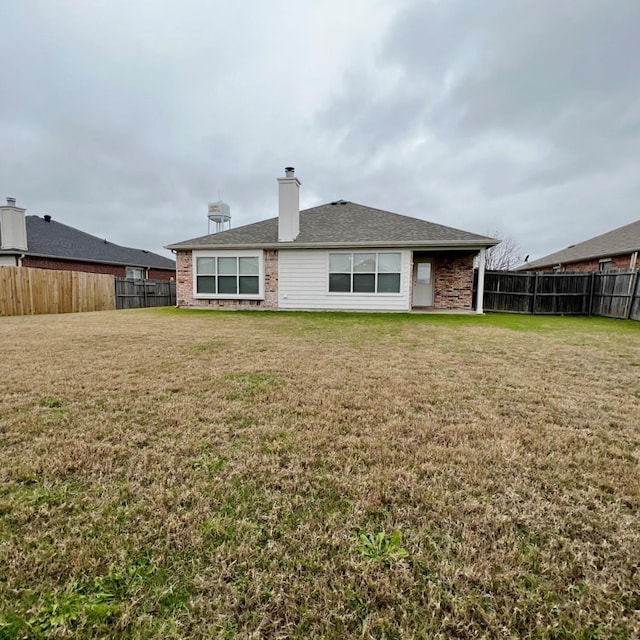 rear view of property featuring brick siding, a lawn, a chimney, and a fenced backyard