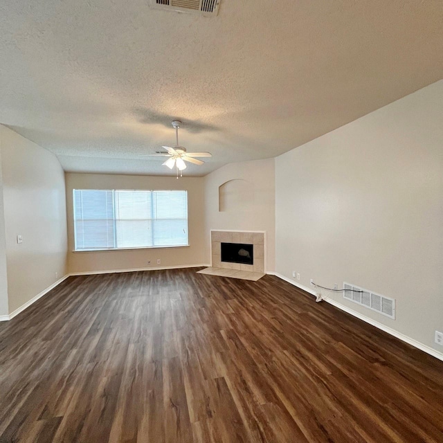 unfurnished living room with visible vents, a tiled fireplace, dark wood-style floors, ceiling fan, and a textured ceiling