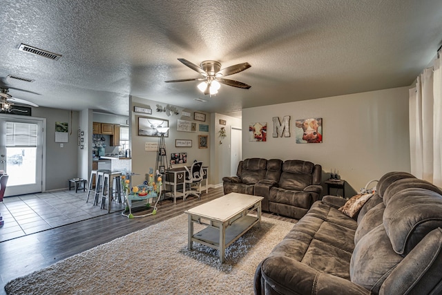 living room with ceiling fan, a textured ceiling, visible vents, and light wood-style floors