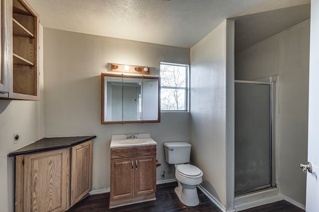 bathroom featuring a stall shower, toilet, wood finished floors, a textured ceiling, and vanity