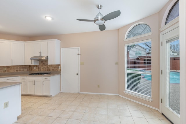 kitchen featuring tasteful backsplash, white cabinets, light countertops, under cabinet range hood, and gas cooktop