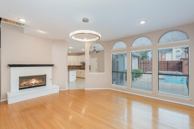 unfurnished living room featuring baseboards, light wood-type flooring, a brick fireplace, and recessed lighting