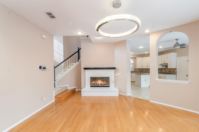 unfurnished living room with visible vents, baseboards, stairs, light wood-style floors, and a brick fireplace