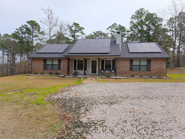 ranch-style home featuring brick siding, a chimney, a porch, a shingled roof, and a front lawn