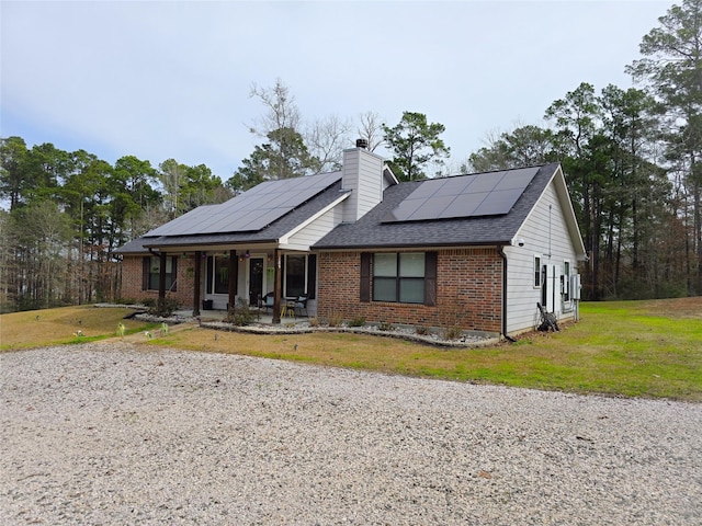 ranch-style house featuring covered porch, brick siding, a shingled roof, a front lawn, and a chimney