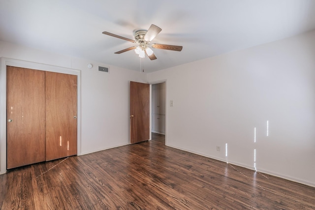 unfurnished bedroom featuring dark wood-type flooring, a closet, visible vents, and a ceiling fan