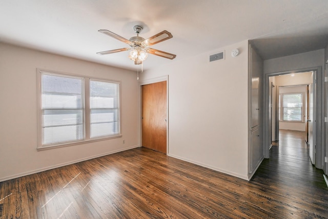 empty room featuring a ceiling fan, baseboards, visible vents, and dark wood-type flooring