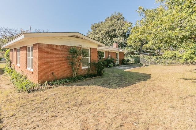 view of property exterior featuring a yard, brick siding, and fence